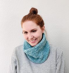 a woman with red hair wearing a blue knitted cowl and smiling at the camera