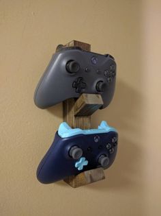 two video game controllers are mounted to a wooden holder on the wall, one has a blue and gray controller attached to it