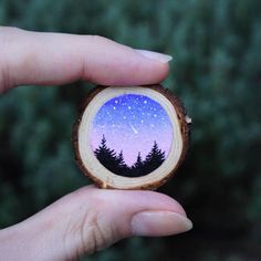 a hand holding a piece of wood with trees on it and the night sky painted on it