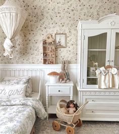 there is a doll in a baby carriage next to the dresser and bed with floral wallpaper