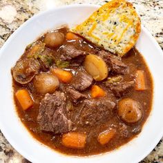 a bowl of beef stew with potatoes and gravy next to a piece of bread