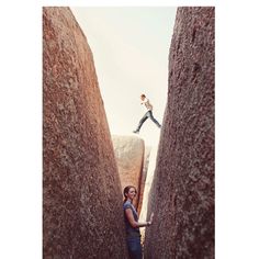 a woman standing between two large rocks with her arms in the air while another person stands on top