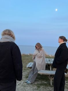 two women sitting on a bench looking at the ocean and one woman standing next to her