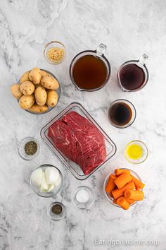 raw meat, potatoes, carrots and other ingredients laid out on a marble surface