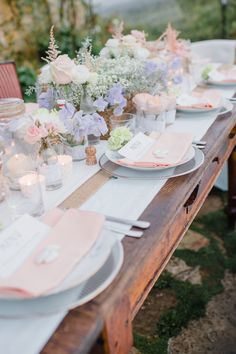 a long table with plates and flowers on it is set for an outdoor dinner party