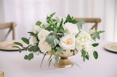 a vase filled with white flowers and greenery on top of a dining room table