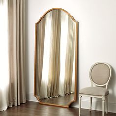 a white chair sitting next to a large mirror on the side of a wall in front of a window