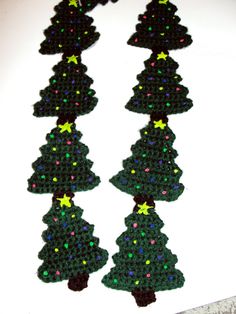 crocheted christmas tree ornaments are displayed on a white surface with green and yellow lights