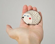 a hand holding a small white and black hedge brooch with red dots on it's face