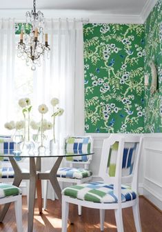 a dining room with green and blue wallpaper, white chairs and a glass table