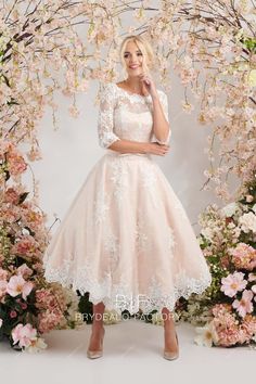 a woman standing in front of a floral arch wearing a pink dress with white lace