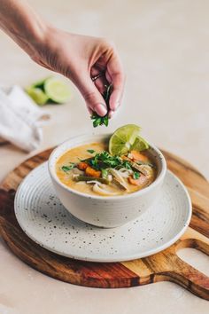 a bowl of soup on a plate with a lime wedged in the top corner