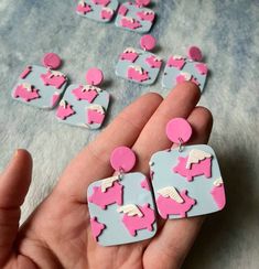 a person holding some pink and blue earrings in their hand on a gray surface with white circles