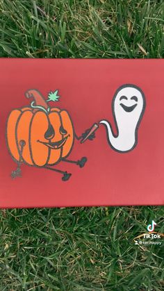 a red box with a cartoon pumpkin and ghost drawn on it sitting in the grass