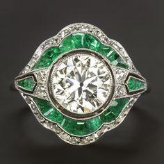 Why we love it:This vintage style diamond ring is gorgeously designed and handcrafted with a dazzling 1.89 carat old cut diamond center and spring green calibre cut emerald accents!Highlights:- 1.89ct EGL-USA certified center diamond- Large spread and a look comparable to a typical 2 carat- Beautiful old transitional cut- Excellent VS2 clarity- Very minimal warmth with J-K color. Faces up nicely white in contrast to the emeralds- Natural emerald accents with bright and vibrant color- Bright whit Heirloom Gia Certified Diamond Ring, Vintage Emerald Diamond Ring With Round Cut, Vintage Green Diamond Ring With Center Stone, Art Deco Round Emerald Ring With Center Stone, Vintage Diamond White Ring With Halo Setting, Vintage Emerald Ring With Brilliant Cut For Gift, Vintage Diamond White Diamond Ring With Halo Setting, Vintage Emerald Ring With Rose Cut Diamonds, Vintage Green Diamond Ring With Accents