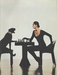 a woman sitting at a table playing chess with a dog