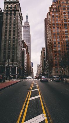 an empty city street with tall buildings and yellow lines painted on the road in front of it