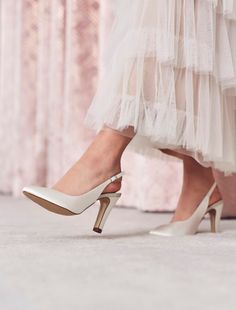 a woman wearing high heels and a white dress is standing in front of a curtain