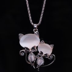 two white cats are sitting on top of a silver plated necklace with crystal stones