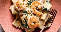 pasta with shrimp, spinach and parmesan cheese on a pink plate next to a fork