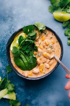 a person holding a spoon in a bowl filled with soup and garnished with cilantro