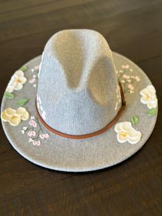 Fedora style hat with textured hand painted flowers.       -Faux leather band with gold buckle detail Material:       -65% Cotton      -35% Polyester Hat measurements:       -2.8" brim      -22.4-23.2" inner circumference      -4.7" height      -Inside circumference is fully ADJUSTABLE - there is a string pull on the inside to adjust to your perfect fit. Care Instructions:      -Spot clean only with damp cloth      -Paint can get wet and will not come off      -Do not put through the washer/dryer Adjustable Short Brim Felt Hat For Spring, Adjustable Brimmed Felt Hat For Spring, Spring Flat Brim Felt Hat, Adjustable Fedora Felt Hat For Spring, Spring Adjustable Fedora Felt Hat, Adjustable Western Felt Hat For Spring, Spring Western Felt Hat With Adjustable Fit, Spring Fedora Felt Hat With Adjustable Fit, Adjustable Brimmed Hat With Floral Print