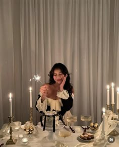 a woman sitting at a table with candles in front of her and some desserts on the table