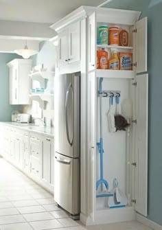 a kitchen with blue walls and white cabinets, including a refrigerator freezer that has cleaning supplies in it