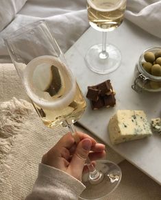 a person holding a wine glass with cheese and olives on the table in front of them