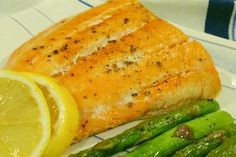 a piece of salmon and asparagus on a white plate with lemon wedges