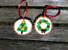 two christmas ornaments are hanging on a wooden bench with red ribbon around the neck and one is decorated like a tree