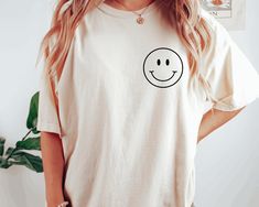 "Smiley Face Comfort Colors Shirt, Happy T-shirt, Smiley Minimal Shirt, Retro Smiley Face Shirt, Smiley Tee, Happy Face Shirt, Gift for Her HOW TO ORDER Please, check and review all photos Choose your size from the drop-down menu and add each shirt to your cart one at a time. Click add to cart. You can go back to add more product Click \"Proceed to check out\" When you check out, you can add a note to the seller for any request Youth, toddler unisex adults round neck shirts are available in all colors listed on the drop-down menu. Designs are printed one color in the front and back of the t-shirt. ALL OF OUR T-SHIRTS ARE FROM U.S.A CARE INSTRUCTIONS Wash inside out, gentle cycle, cold water, tumble dry low, medium iron PRODUCTION AND SHIPPING Processing is 1-3 days. First Class Shipping is Everyday Funny Print Crew Neck Shirt, Everyday Crew Neck Shirt With Funny Print, Funny White T-shirt With Smiley Face, Cute White T-shirt With Smiley Face, Funny White Everyday Top, Funny White Top For Everyday, Fun Crew Neck Top With Smiley Face, Smiley Face Graphic Tee With Short Sleeves, Fun Smiley Face Crew Neck Top