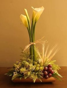 a vase filled with flowers and fruit on top of a wooden table next to a wall