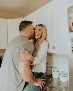 a man and woman are hugging in the kitchen while they stand next to each other