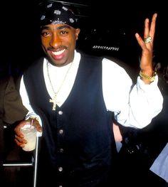 a man in a black vest and hat holding up his peace sign with both hands