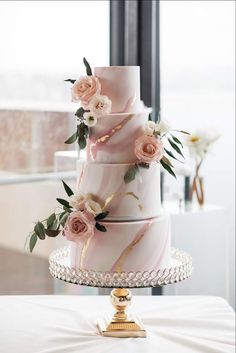 a three tiered cake with pink marble and flowers on the top is sitting on a table