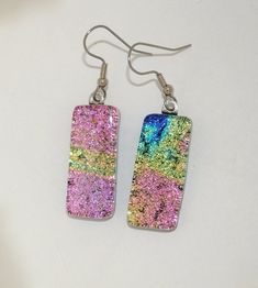 "Gorgeous dichroic glass really stands out in these earrings!  Made from a layering technique I have been experimenting with in my Miami Beach studio,  the results have been coming out unique and interesting!  As is the property of dichroic glass, depending on how the light hits it, it can actually change colors!  Here you see pink color, some blue and yellow.  One-of-a-kind, signed and dated. Measures:  1 1/8\" tall and a little more than 1/2\" wide." Iridescent Glass Earrings For Gift, Iridescent Czech Glass Earrings For Gift, Beach Studio, Sparkle Earrings, Dichroic Glass, Blue Earrings, Miami Beach, Yellow Blue, Fused Glass