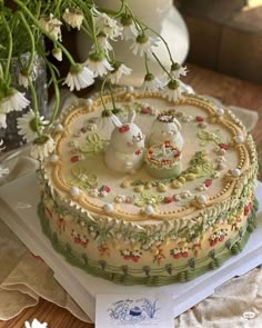 there is a cake decorated with flowers and two rabbits on the top, sitting on a table