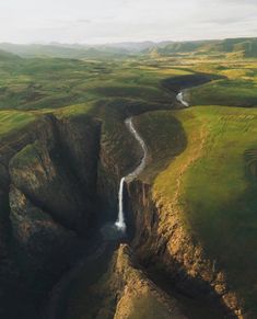 an aerial view of a waterfall in the middle of a green valley with mountains and grass