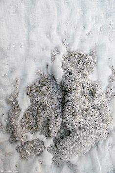 a teddy bear made out of beads on a white fabric with silver sequins