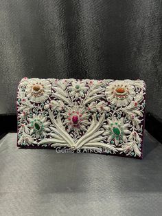 Beautiful hand-embroidered floral silk clutch bag inlaid with semi-precious stones. The front is completely covered in the design and has a closure flap with magnettic snap fastening. This clutch is perfect for daytime or night time. It is the ideal size for fitting all your essentials. It is a stylish accessory for each & every occasion. This equisite piece is even ideal for gifting to your near & dear one's . Thread - Silk Fabric - Velvet Variety of Semi-precious stones are used in this piece Zardozi is a type of heavy and elaborate metal embroidery on silk, satin, or velvet fabric base. Designs are often created using gold and silver wires and can incorporate pearls, beads, and precious stones. The embroidered silk clutch bag is made in Agra, India & is fully handmade. Designed to compl Luxury Bags With Intricate Embroidery For Festive Occasions, Luxury Festive Bag With Intricate Embroidery, Festive Formal Clutch With Intricate Embroidery, Luxury Festive Bags With Intricate Embroidery, Traditional Embellished Clutch For Festivals, Embellished Evening Bag For Festivals And Receptions, Festive Embellished Evening Bag For Receptions, Elegant Embellished Embroidered Fabric For Festivals, Traditional Embroidered Evening Bag For Formal Occasions