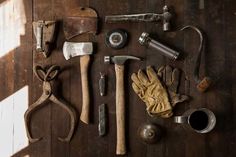 several different tools are laid out on a wooden surface, including hammers and gloves