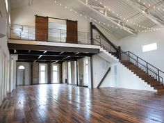 an empty room with wooden floors and stairs leading to the second floor that is decorated with string lights