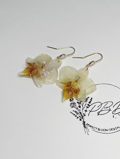 two white flowers with yellow centers are hanging from gold - plated earwires