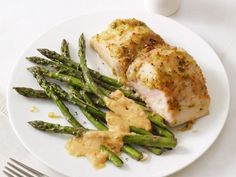 two pieces of chicken and asparagus on a white plate with mustard sauce next to it