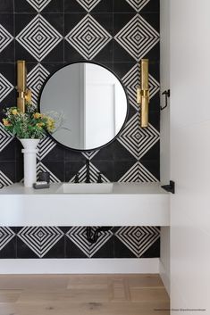 a bathroom with black and white tiles on the wall, gold faucets and a round mirror