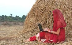 a woman sitting in front of a pile of hay using a laptop computer on her lap