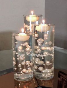 two glass vases filled with pearls and lit candles