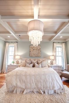 a large white bed sitting under a chandelier in a bedroom