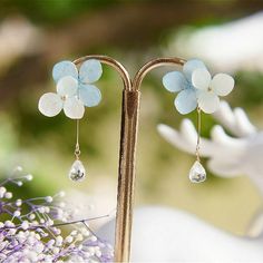 a pair of earrings with flowers hanging from it's ear posts in front of purple flowers